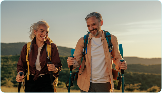 Couple hiking at altitude with trekking poles on a mountain trail.