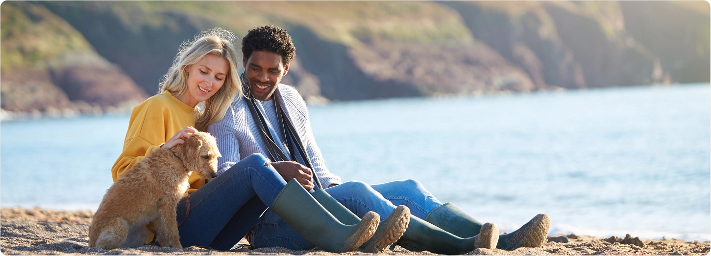 male and female couple sitting on a beach with their dog